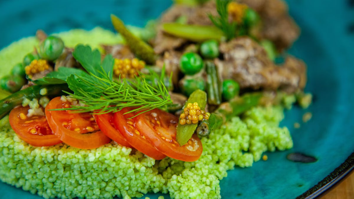 Close-up of a colorful green couscous salad with tomatoes and fresh herbs.